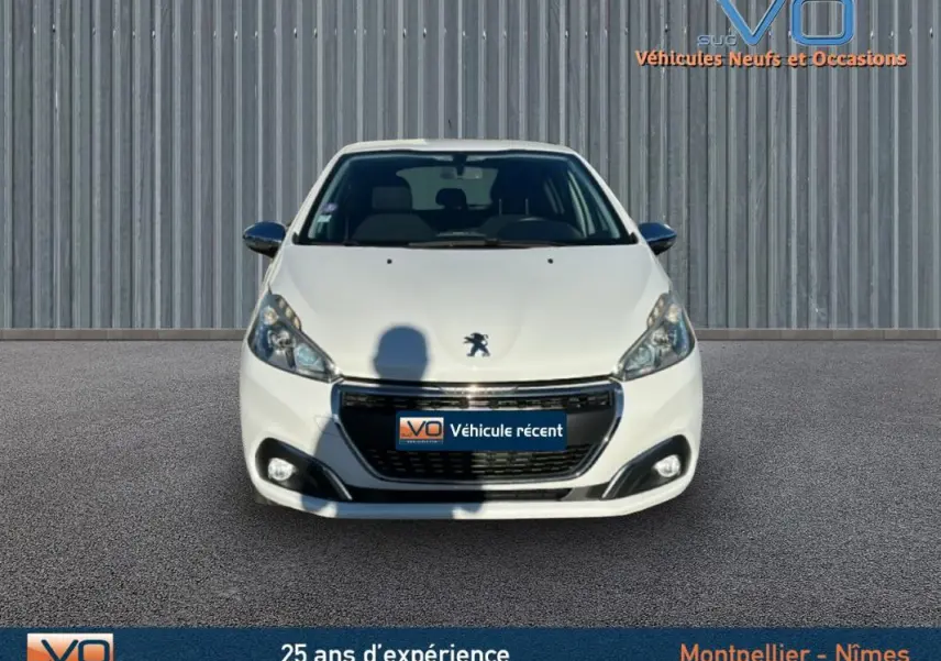 Vue avant d'une Peugeot 208 blanche de 2015, avec phares allumés et calandre noire brillante sur fond neutre.