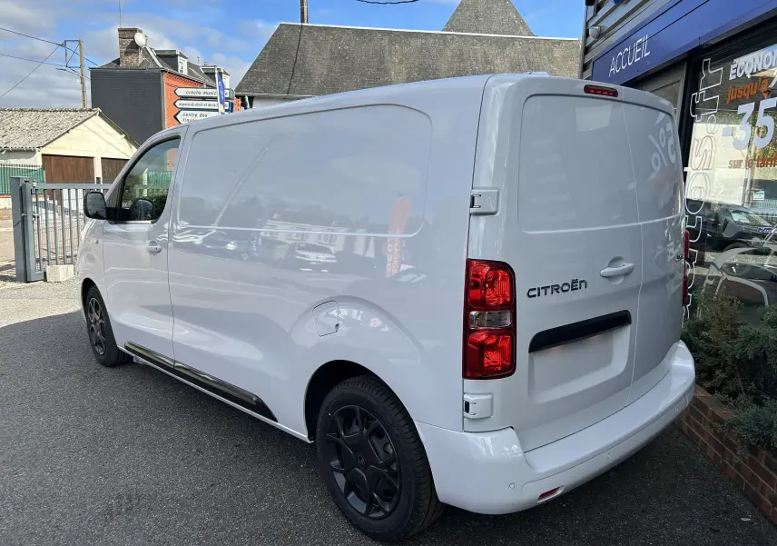 Vue 3/4 arrière droite d’un Citroën Jumpy blanc, fourgon utilitaire avec feux arrière rouges et jantes noires.