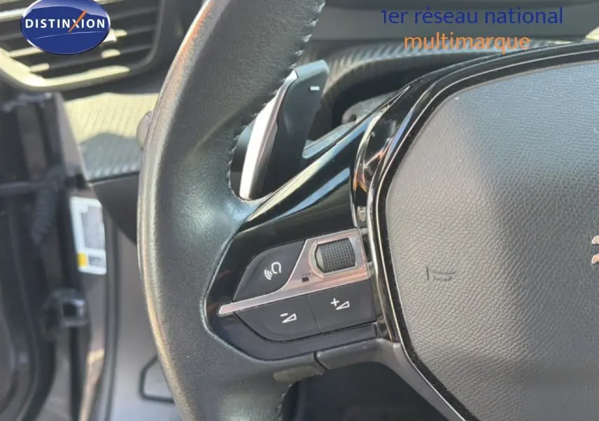 Gros plan sur le volant noir de la Peugeot 2008 1.2 PureTech 130, montrant les commandes audio et de volume.
