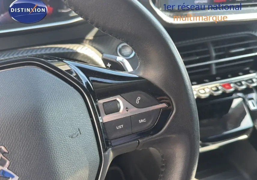 Gros plan sur le volant cuir noir du Peugeot 2008 2020, mettant en valeur les commandes intégrées et la console centrale en arrière-plan.