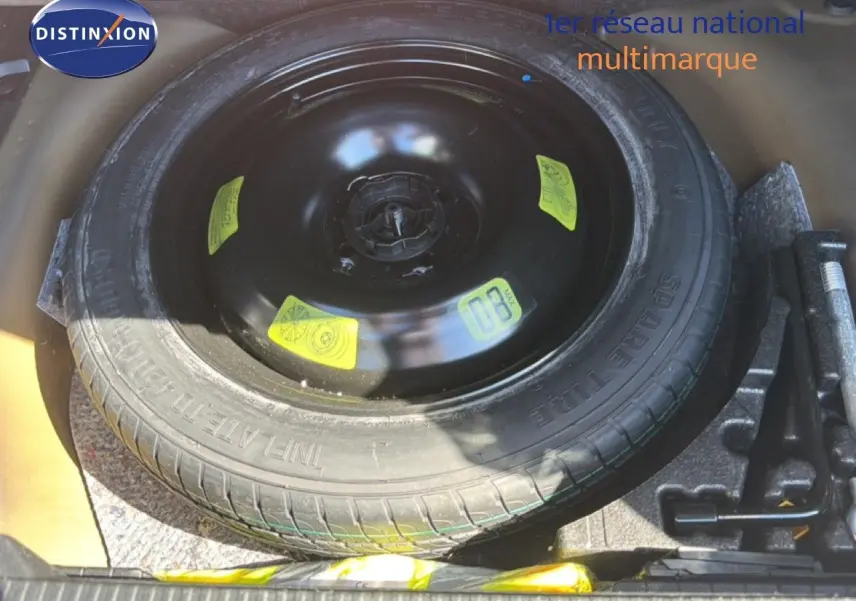 Vue rapprochée de la roue de secours noire dans le coffre d'une Peugeot 2008 gris platinium, avec outils de changement visibles.