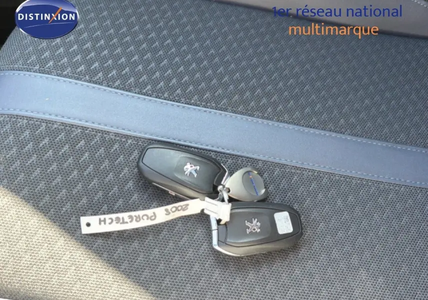Clé de voiture Peugeot 2008 posée sur un siège tissu gris avec surpiqûre bleue, vue en gros plan.