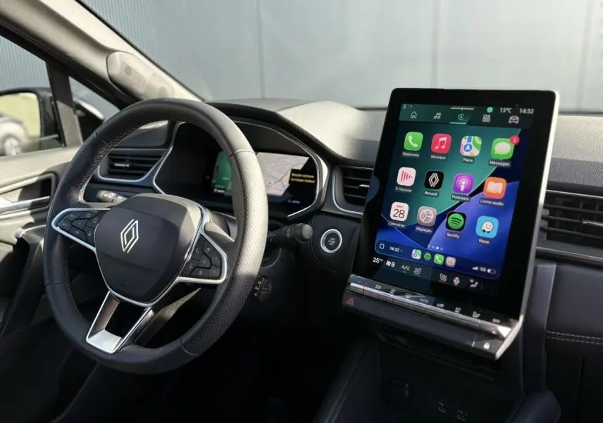 Vue intérieure côté conducteur du Renault SYMBIOZ 2025, avec volant noir et grand écran tactile central allumé.
