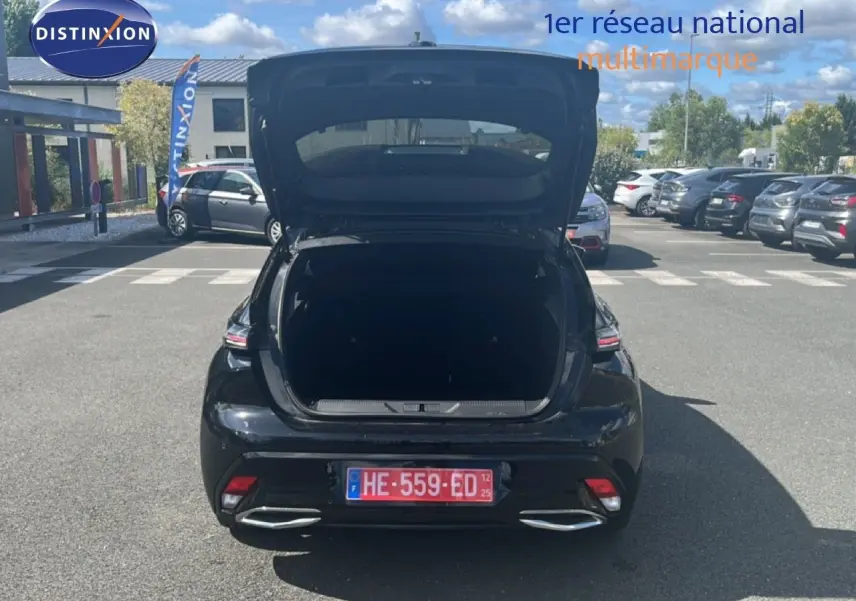 Vue arrière d'une Peugeot 308 Hybrid 145ch noire métal avec coffre ouvert sur un parking en extérieur.