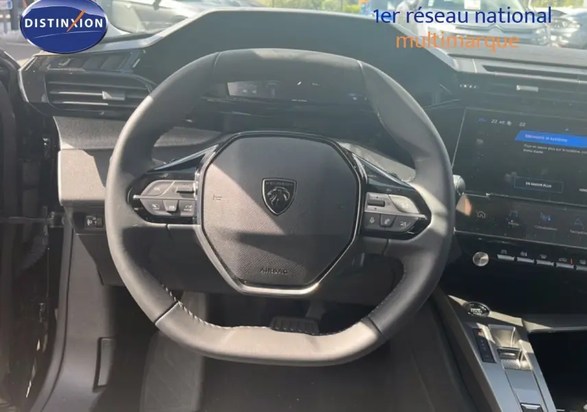 Vue intérieure centrée sur le volant noir de la Peugeot 308 Hybrid 2025 avec tableau de bord et écran tactile visibles.