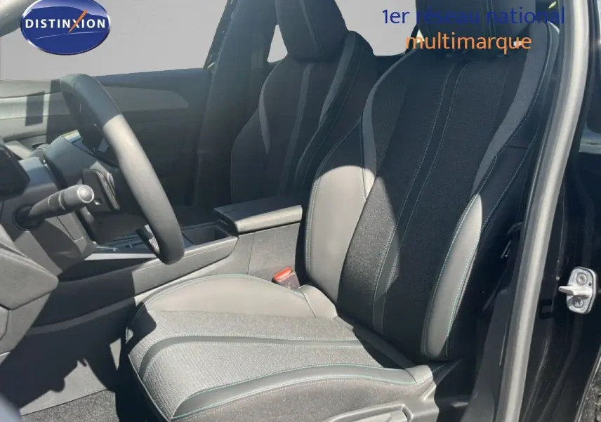 Intérieur de la Peugeot 308 Hybrid 2025 vu côté conducteur, sièges tissu et cuir gris noir avec surpiqûres vertes.