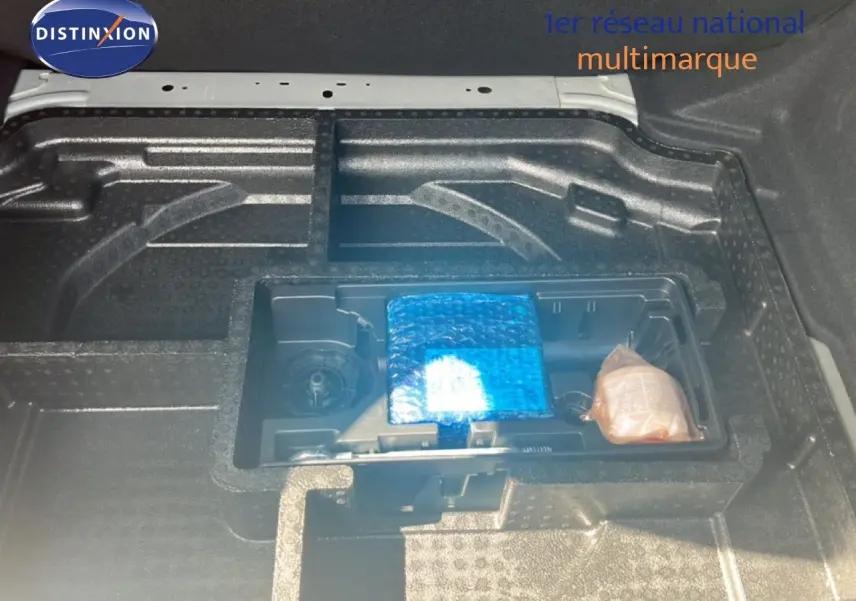 Coffre ouvert d'une Peugeot 308 noir métal, montrant le rangement sous plancher avec accessoires emballés.