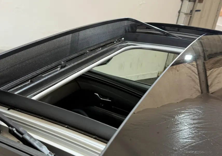 Toit ouvrant panoramique ouvert sur Hyundai Tucson noir, vue rapprochée sur l'ouverture et l'intérieur côté conducteur.