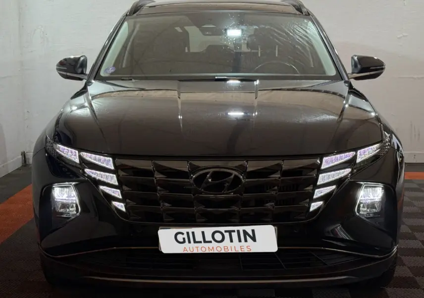 Vue frontale d'un Hyundai Tucson noir avec phares LED allumés et calandre imposante en intérieur showroom.