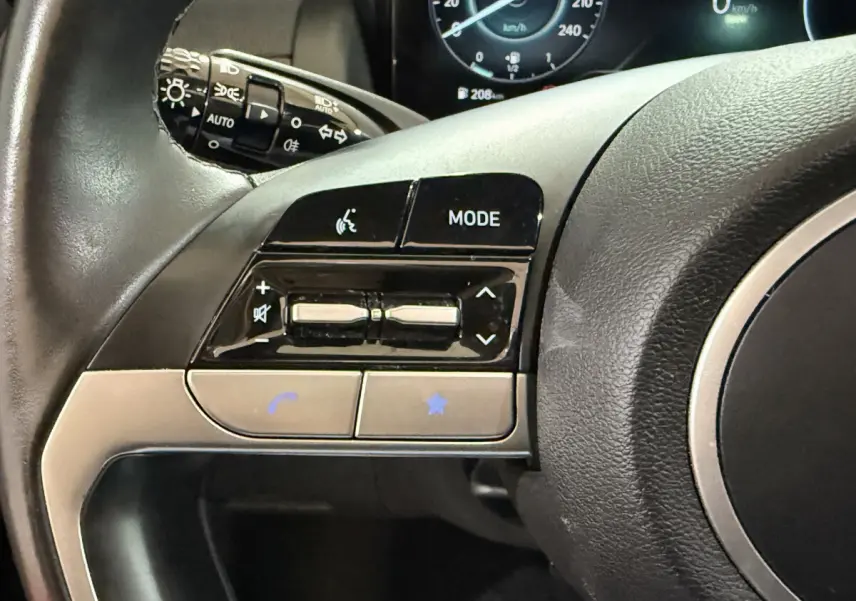 Gros plan sur les commandes gauche du volant noir du Hyundai Tucson 2021, avec tableau de bord numérique en arrière-plan.