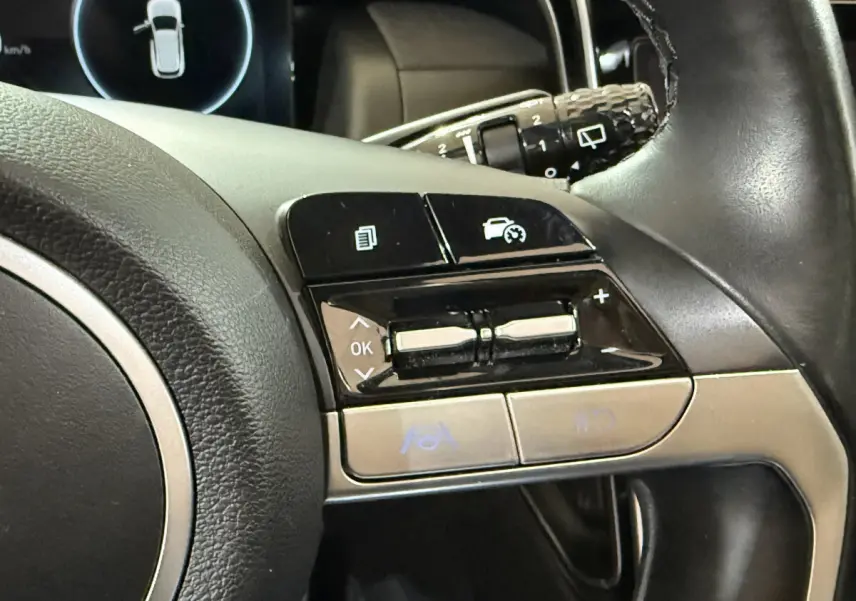 Gros plan sur les commandes du volant cuir noir du Hyundai Tucson 2021, avec boutons multifonctions et régulateur de vitesse.