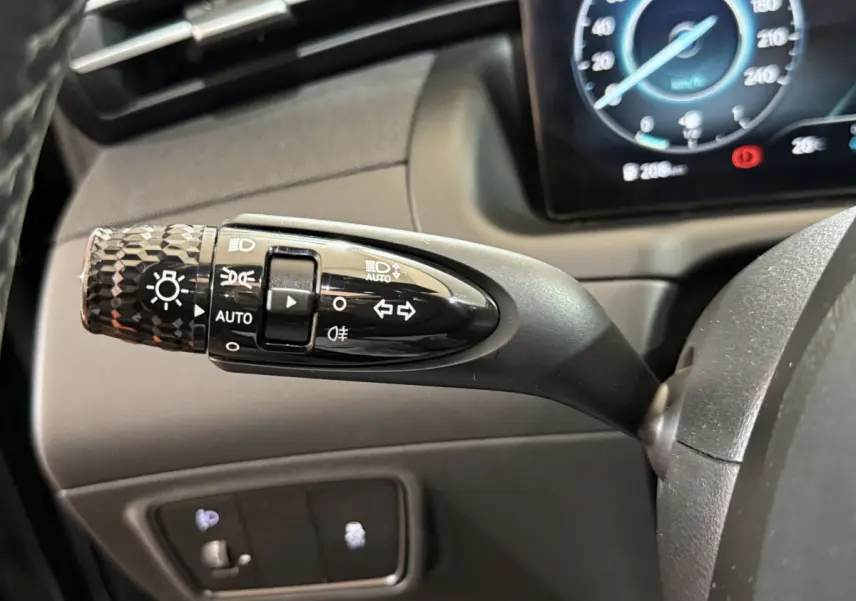 Gros plan sur la commande des phares et clignotants du Hyundai Tucson 2021, avec tableau de bord numérique en arrière-plan.