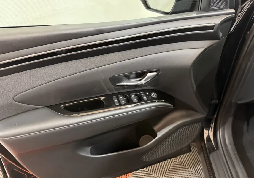 Vue intérieure du panneau de porte côté conducteur du Hyundai Tucson noir, avec commandes électriques et poignée argentée.