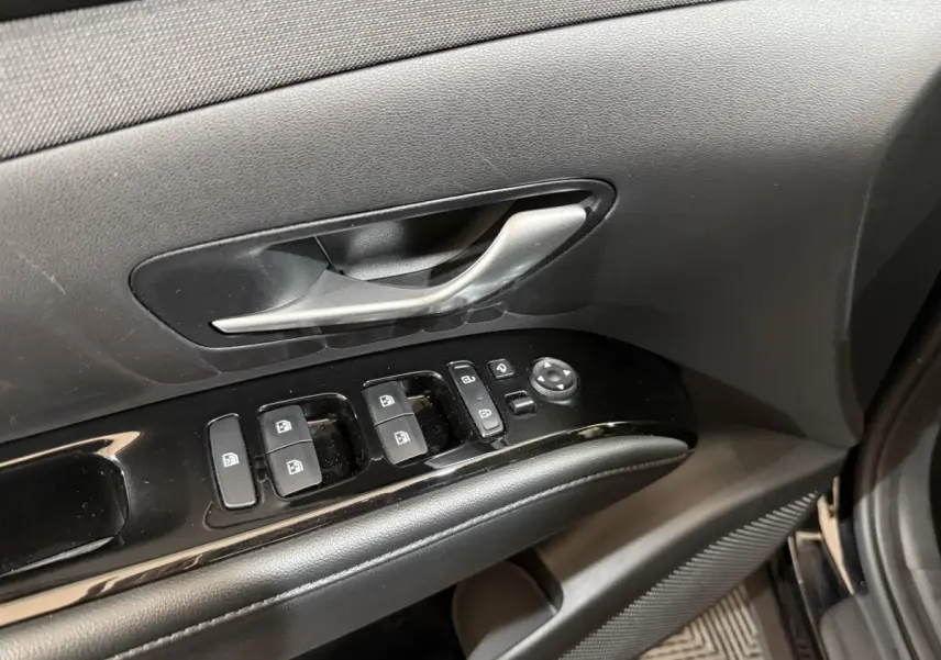 Gros plan sur la porte côté conducteur du Hyundai Tucson noir 2021, montrant les commandes des vitres et la poignée intérieure argentée.
