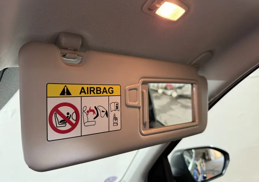 Pare-soleil côté conducteur beige avec miroir intégré et avertissement airbag, rétroviseur extérieur noir visible sur Hyundai Tucson 2021.