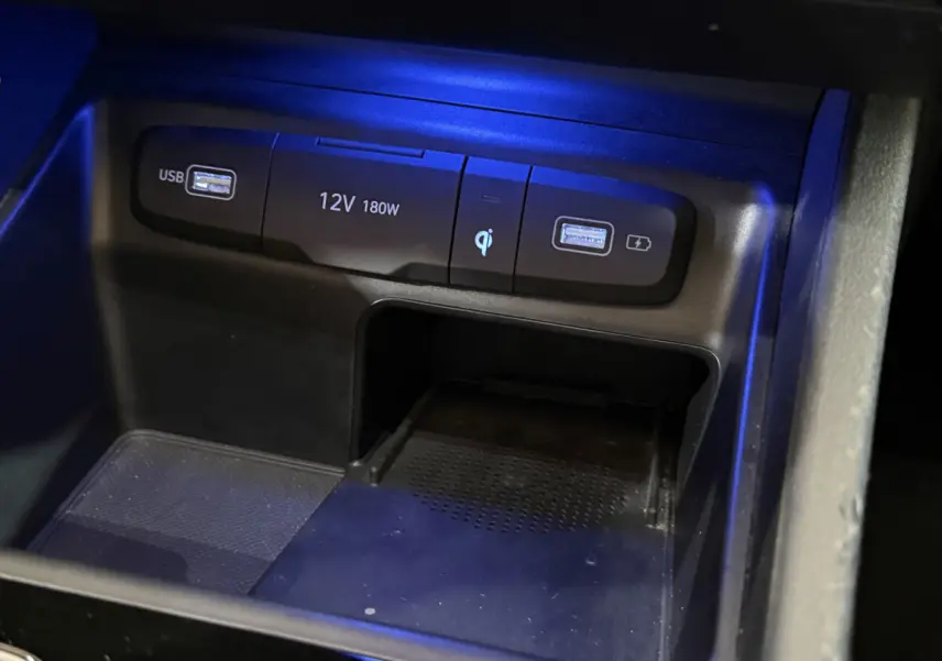 Gros plan sur la console centrale noire du Hyundai Tucson 2021 avec ports USB, prise 12V et chargeur à induction éclairés en bleu.