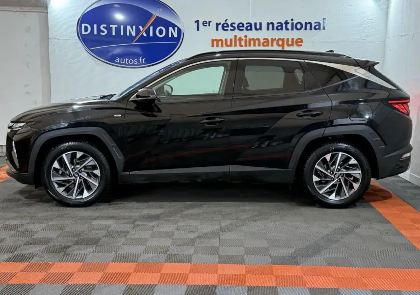 Profil côté gauche d'un Hyundai Tucson noir 2021 hybride, avec jantes alliage et feux arrière LED visibles en intérieur showroom.