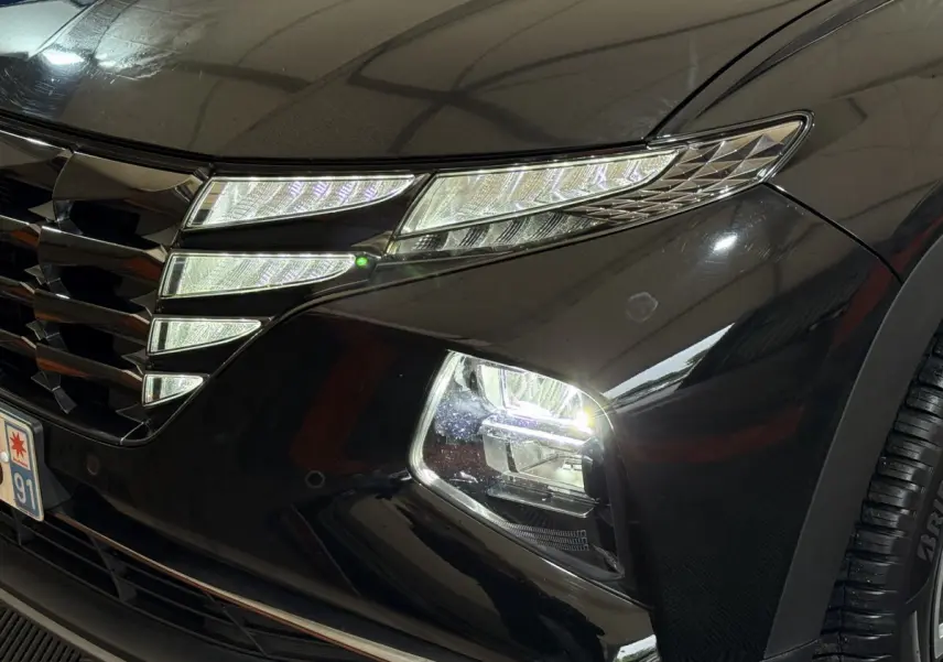 Gros plan sur le phare avant droit allumé d'un Hyundai Tucson noir, mettant en valeur la calandre et les LED distinctives.