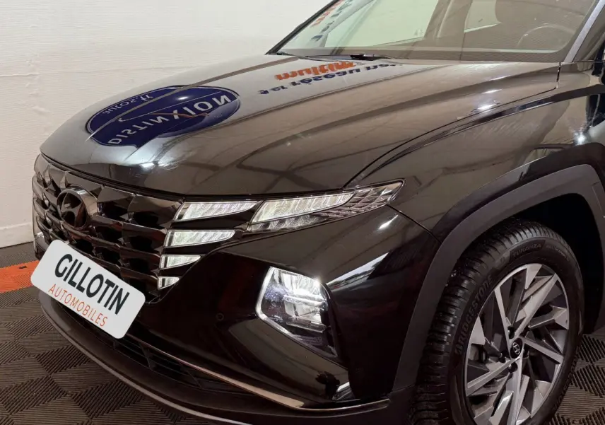 Vue 3/4 avant droite du Hyundai Tucson noir avec calandre distinctive et phares LED allumés.