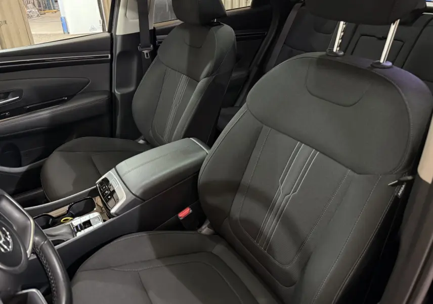 Vue intérieure côté avant gauche du Hyundai Tucson 2021, sièges noirs en tissu et console centrale avec commandes.