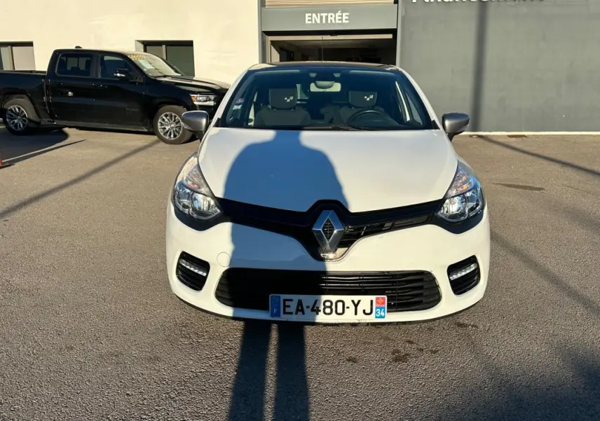 Renault Clio IV TCe 120 GT EDC blanc vue de face, avec calandre noire et feux avant allumés.