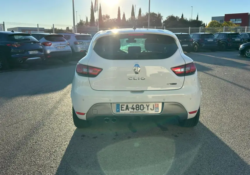 Vue arrière d'une Renault Clio IV TCe 120 GT blanche garée en extérieur avec feux arrière allumés et double sortie d'échappement.