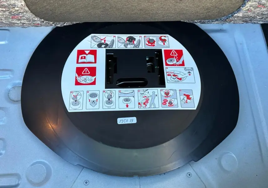 Gros plan sur la roue de secours noire avec instructions d'utilisation dans le coffre d'une Renault Clio IV blanche.