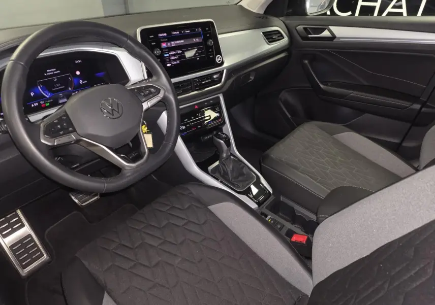 Intérieur avant du Volkswagen T-Roc 2025, sièges tissu noir/gris, tableau de bord gris étain avec écran tactile 8 pouces.