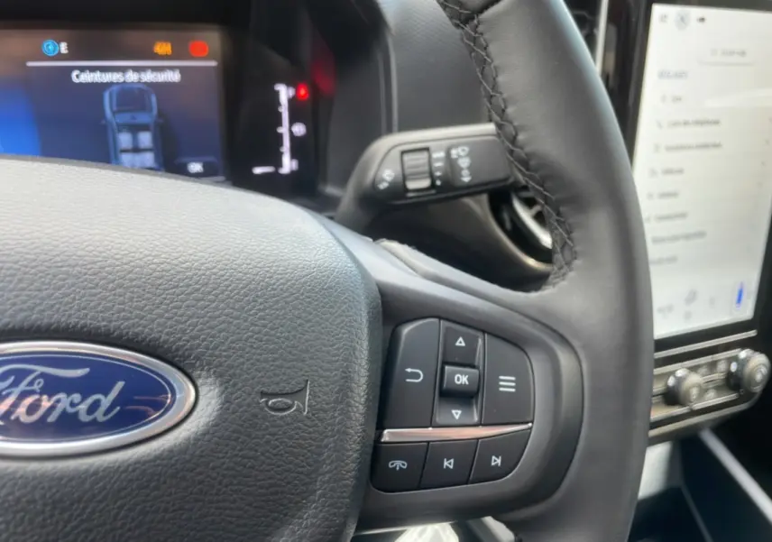 Vue rapprochée du volant cuir du Ford Ranger rouge 2025 avec commandes multifonctions et tableau de bord digital.