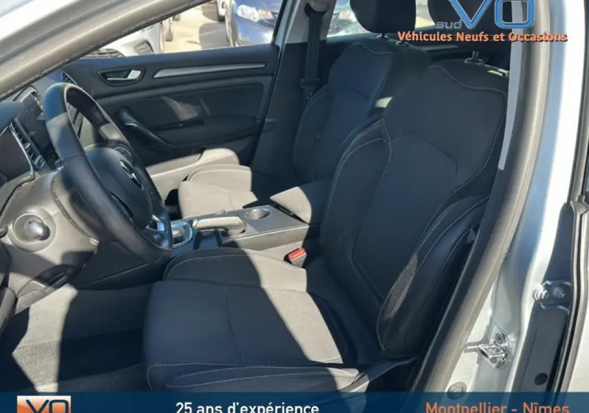 Vue intérieure côté conducteur de la Renault Mégane IV Berline gris clair, sièges noirs et tableau de bord visible.