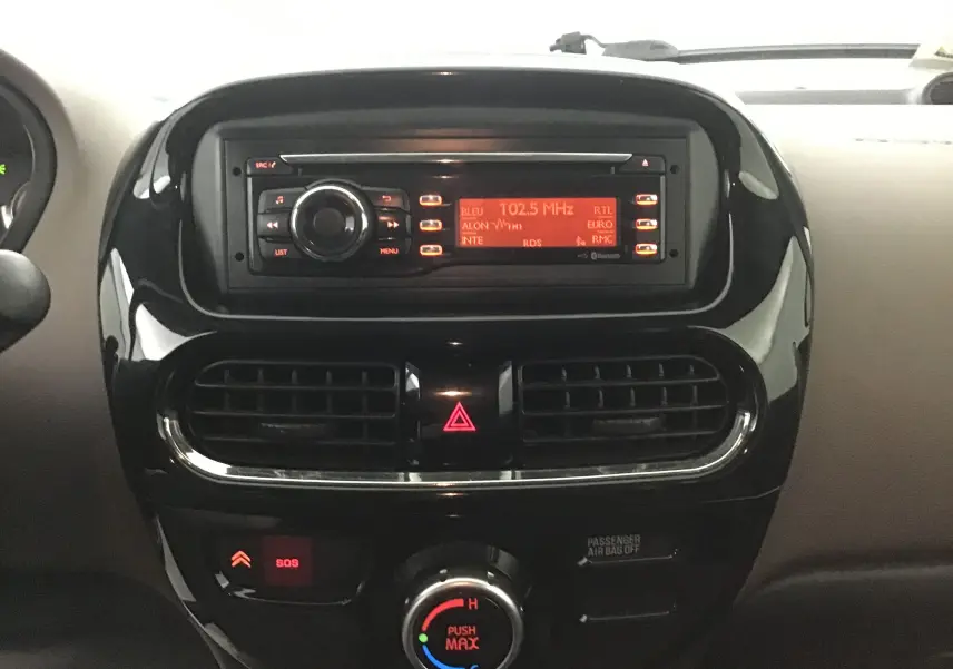 Tableau de bord noir brillant de la Citroën C-ZERO 2018, avec radio allumée et commandes de climatisation visibles.