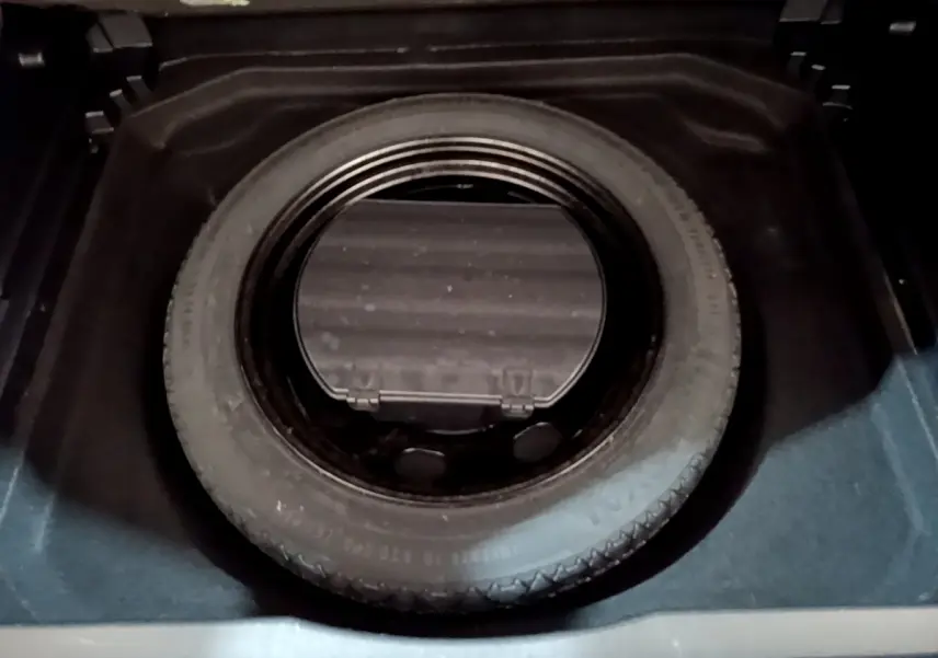 Gros plan sur la roue de secours noire logée dans le coffre d'un Citroën C5 Aircross gris foncé.