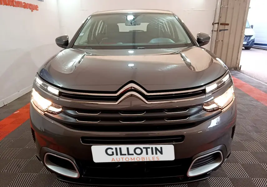 Vue avant d'un Citroën C5 Aircross gris foncé avec feux allumés et calandre chromée dans un garage.