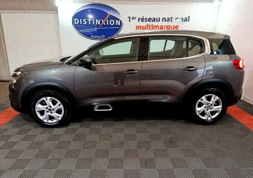 Profil côté gauche du SUV Citroën C5 Aircross gris foncé avec jantes alliage 17 pouces en intérieur showroom.