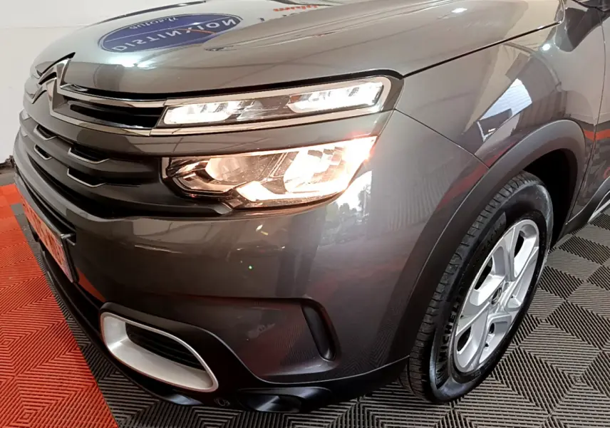 Vue 3/4 avant droit du Citroën C5 Aircross gris foncé avec feux allumés et jantes alliage 17 pouces.