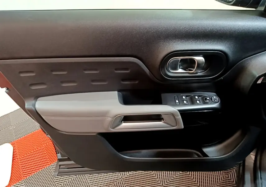 Gros plan sur la porte côté gauche du Citroën C5 Aircross gris foncé, avec accoudoir gris clair et commandes électriques.