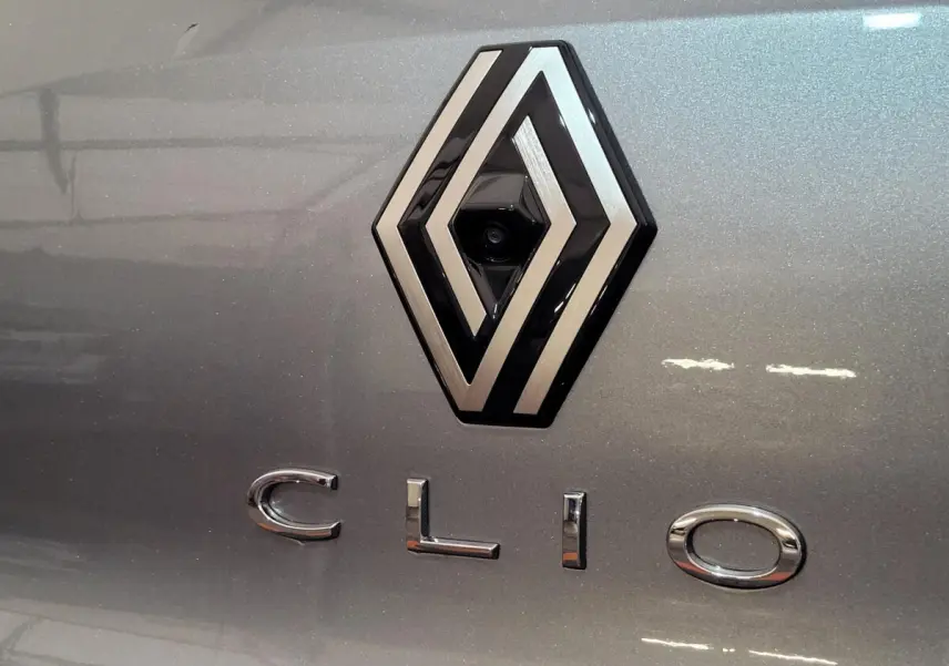 Gros plan sur le logo Renault et l'inscription Clio en chrome sur la carrosserie gris foncé métallisée.