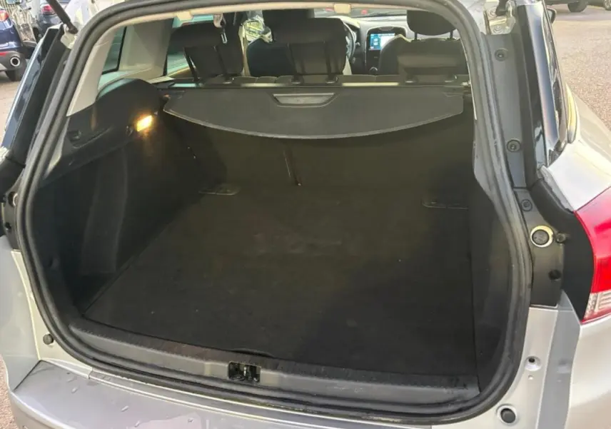 Coffre ouvert vu de l'arrière d'une Renault Clio IV Estate gris clair, montrant l'espace de chargement et la plage arrière.