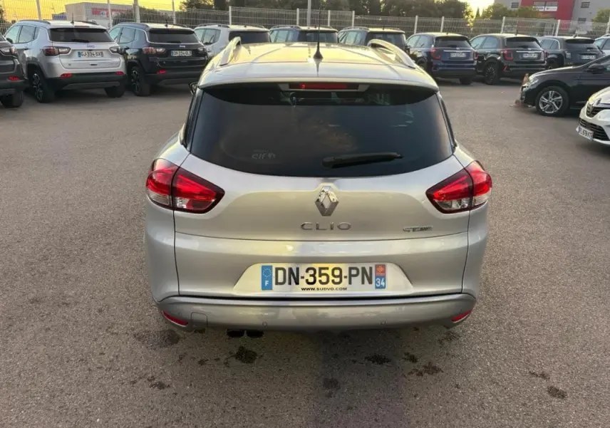 Vue arrière d'une Renault Clio IV Estate gris clair avec vitres surteintées et feux arrière allumés sur parking.