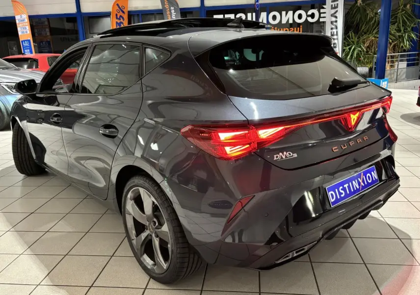 Vue 3/4 arrière droite d'une CUPRA Leon gris Graphène avec feux arrière allumés et jantes alliage 5 branches.