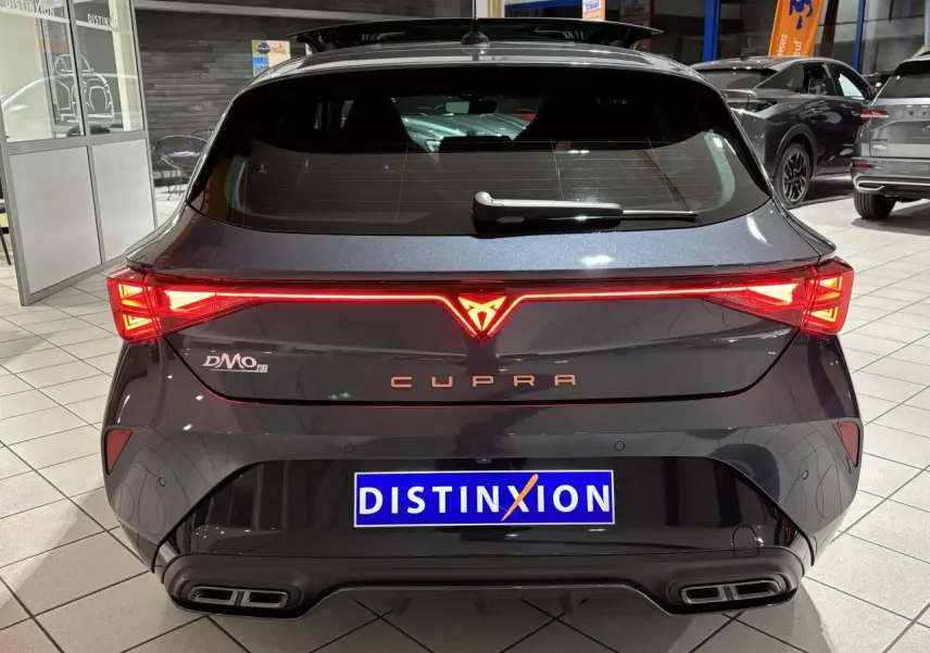 Vue arrière d'une CUPRA Leon gris Graphène avec feux arrière Tri-LED allumés et double sortie d'échappement noire stylisée.