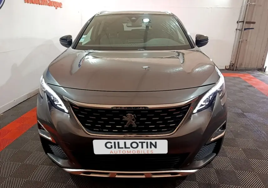 Vue avant d'un Peugeot 3008 gris foncé avec calandre noire et phares LED allumés dans un showroom.