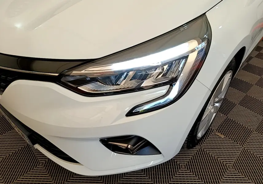 Gros plan sur l'avant droit blanc d'une Renault Clio 2020, mettant en valeur le phare LED et la jante alliage.