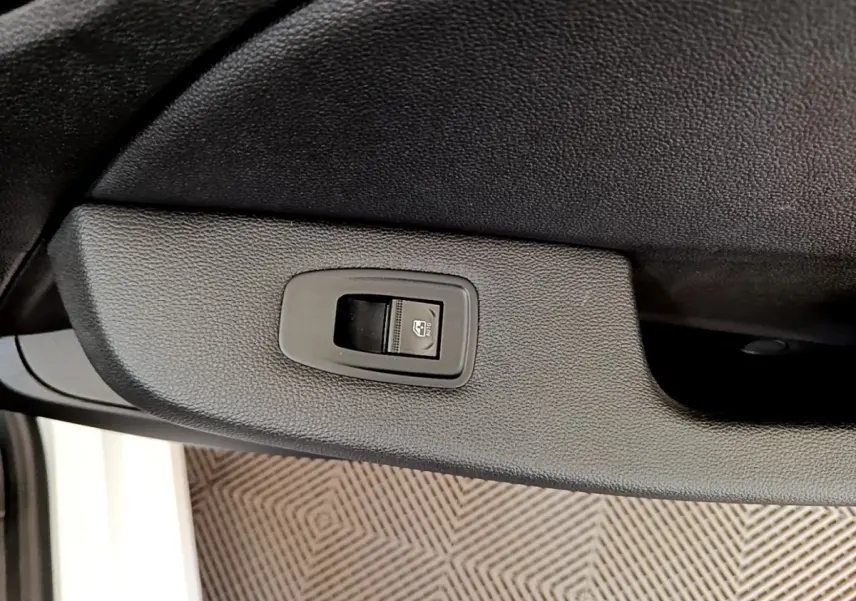 Gros plan sur le bouton de commande de la vitre électrique côté conducteur d’une Renault Clio Business Blue dCi blanche.