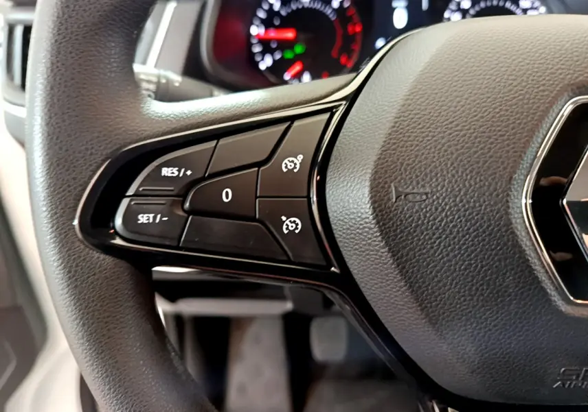 Gros plan sur le volant noir du Renault Trafic Fourgon 2022 avec commandes de régulateur de vitesse et tableau de bord flou.