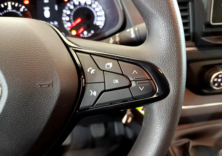 Gros plan sur les commandes multifonctions du volant noir du Renault Trafic Fourgon 2022, avec tableau de bord en arrière-plan flou.