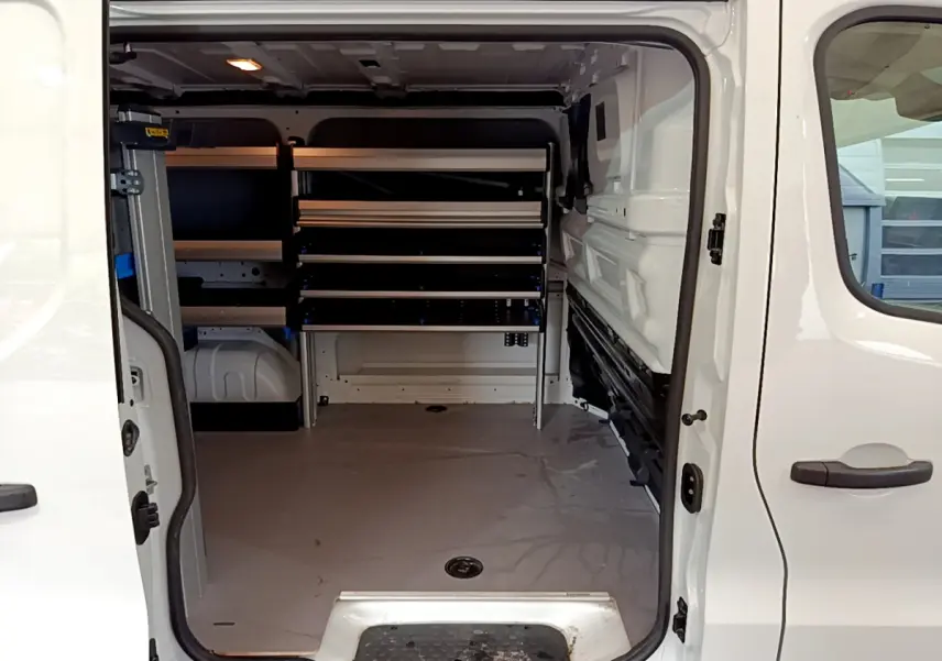 Vue intérieure du Renault Trafic Fourgon blanc 2022, montrant l'espace de chargement avec étagères métalliques sur le côté gauche.
