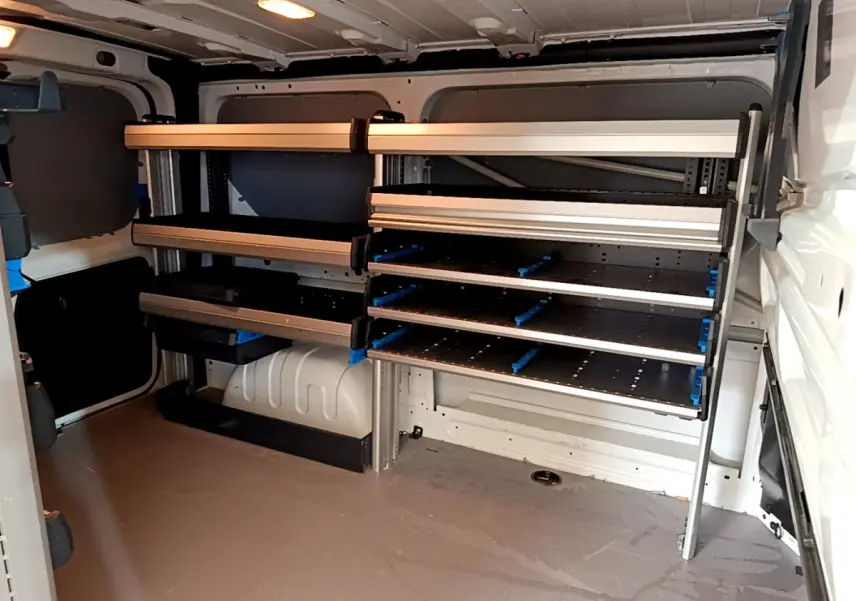 Intérieur du fourgon Renault Trafic blanc vu de l'arrière, avec étagères métalliques et espace de chargement aménagé.
