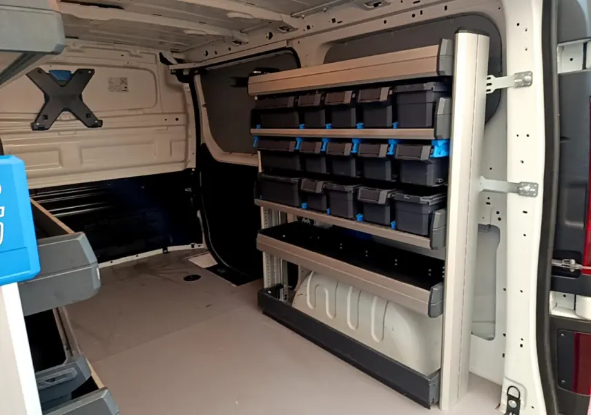 Intérieur du fourgon Renault Trafic blanc vu de l'arrière, avec étagères et rangements modulaires sur le côté droit.