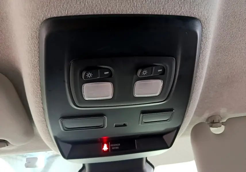 Vue en gros plan du plafonnier intérieur noir avec commandes d'éclairage et témoin airbag passager allumé du Renault Trafic blanc.